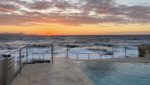 Ein Poolbereich mit Blick auf das Meer und einen Sonnenuntergang.