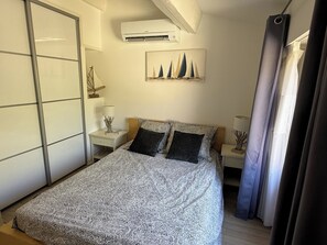 A bedroom with a bed, nightstands, an air conditioning unit, a painting, and a curtain. - Superb villa "feet in the water"  (Roquebrune-Sur-Argens)