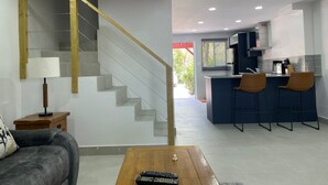 Un salon moderne avec un escalier, une table basse et un canapé. Il y a également un coin cuisine avec des tabourets de bar et une table à manger.