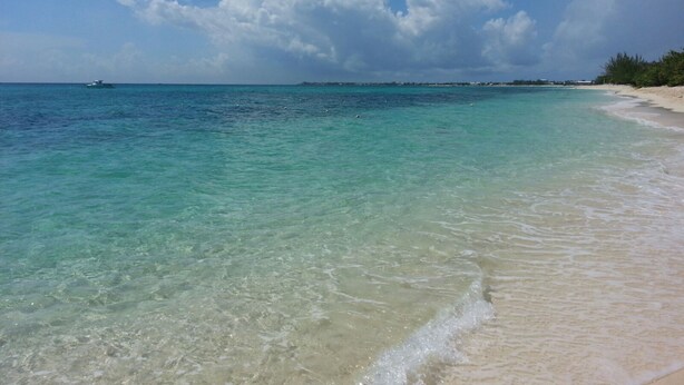 Une plage à l’eau turquoise et limpide, un rivage sablonneux et une île qui se dessine à l’horizon.