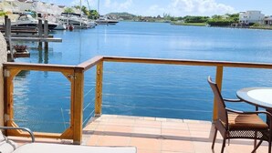 Une terrasse avec vue sur un port de plaisance, un fauteuil, une table et une rambarde en bois.