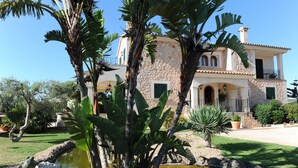 Un'ampia casa in pietra con facciata in pietra, un cortile centrale e un piccolo stagno.