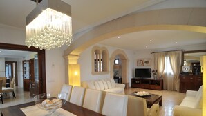 Un soggiorno ampio con soffitto alto, un lampadario, un divano, una televisione e un'area pranzo con tavolo e sedie.