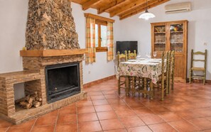 Un comedor con chimenea, vigas de madera en el techo, suelo de baldosas, una mesa preparada para cuatro personas y un aparador con puertas de cristal.
