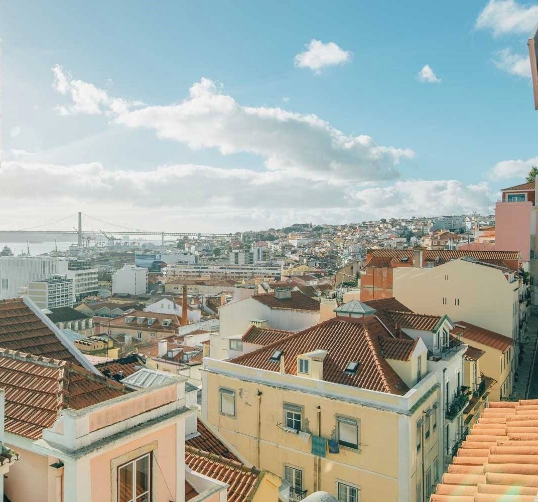 A cityscape with a view of the sea and a bridge in the distance.