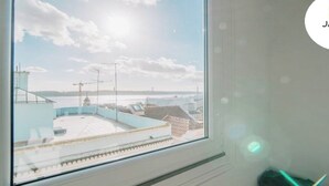 Een kamer met een groot raam dat uitkijkt over een kustgebied met gebouwen en water.