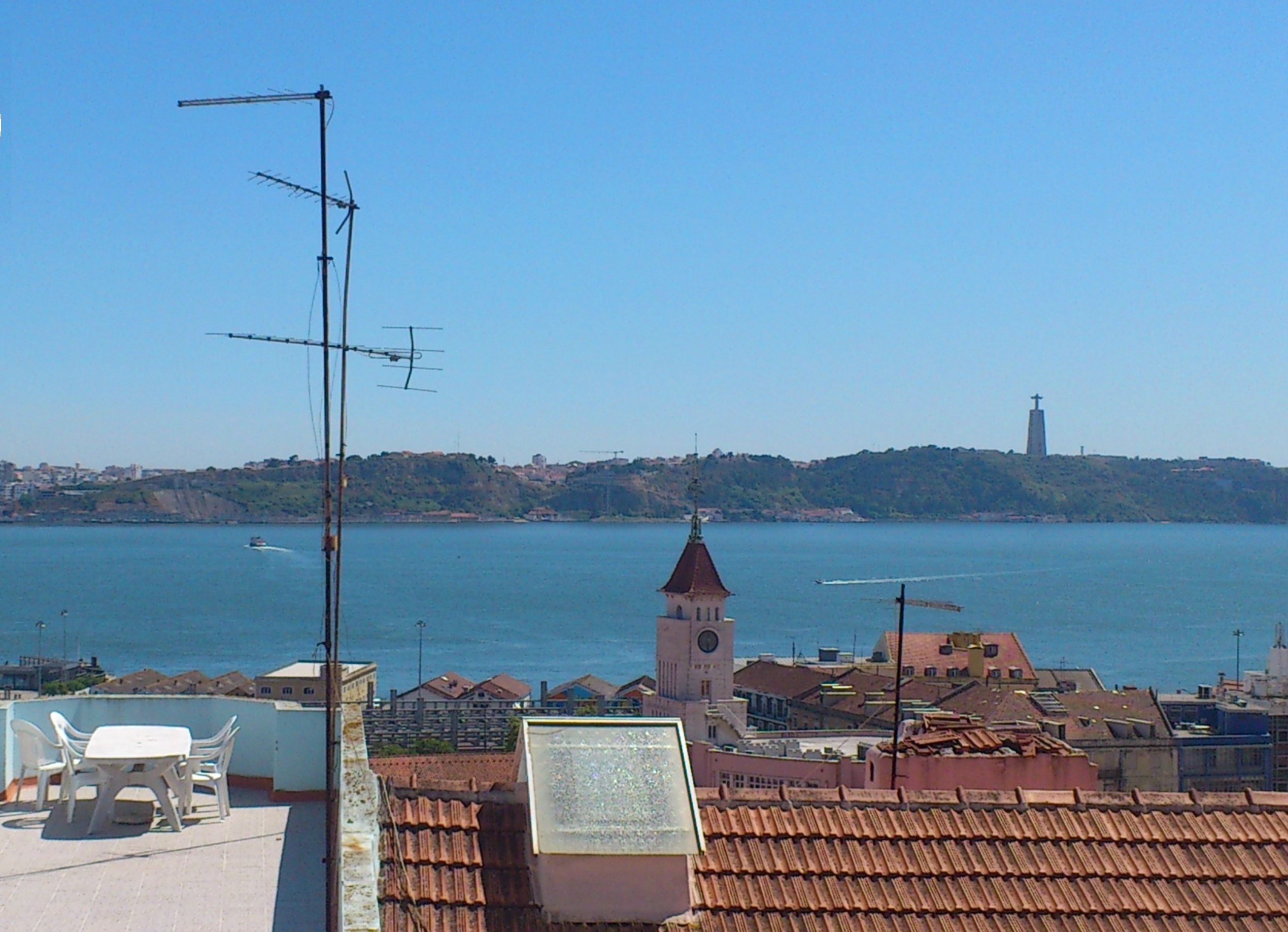 Un paisaje urbano costero con vista despejada al mar, una torre de iglesia destacada y un logotipo en la esquina superior izquierda.