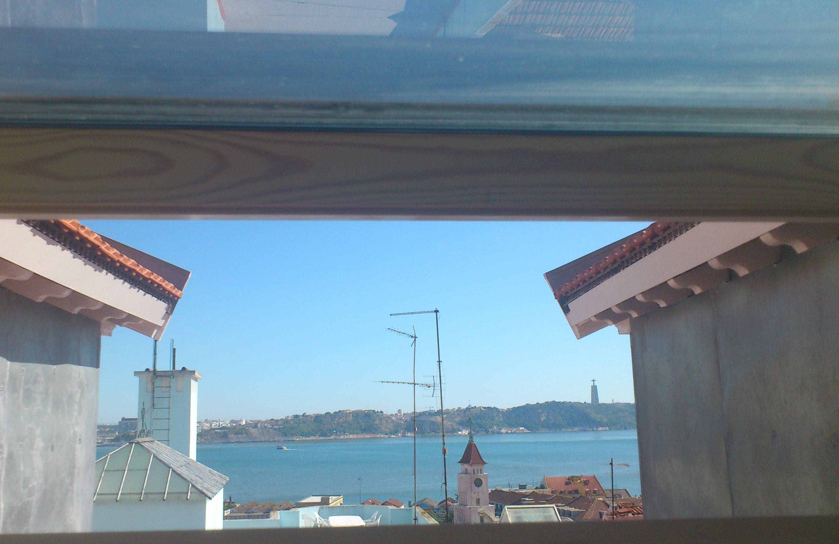 A view from a window overlooking a coastal town with buildings and a clear sky.