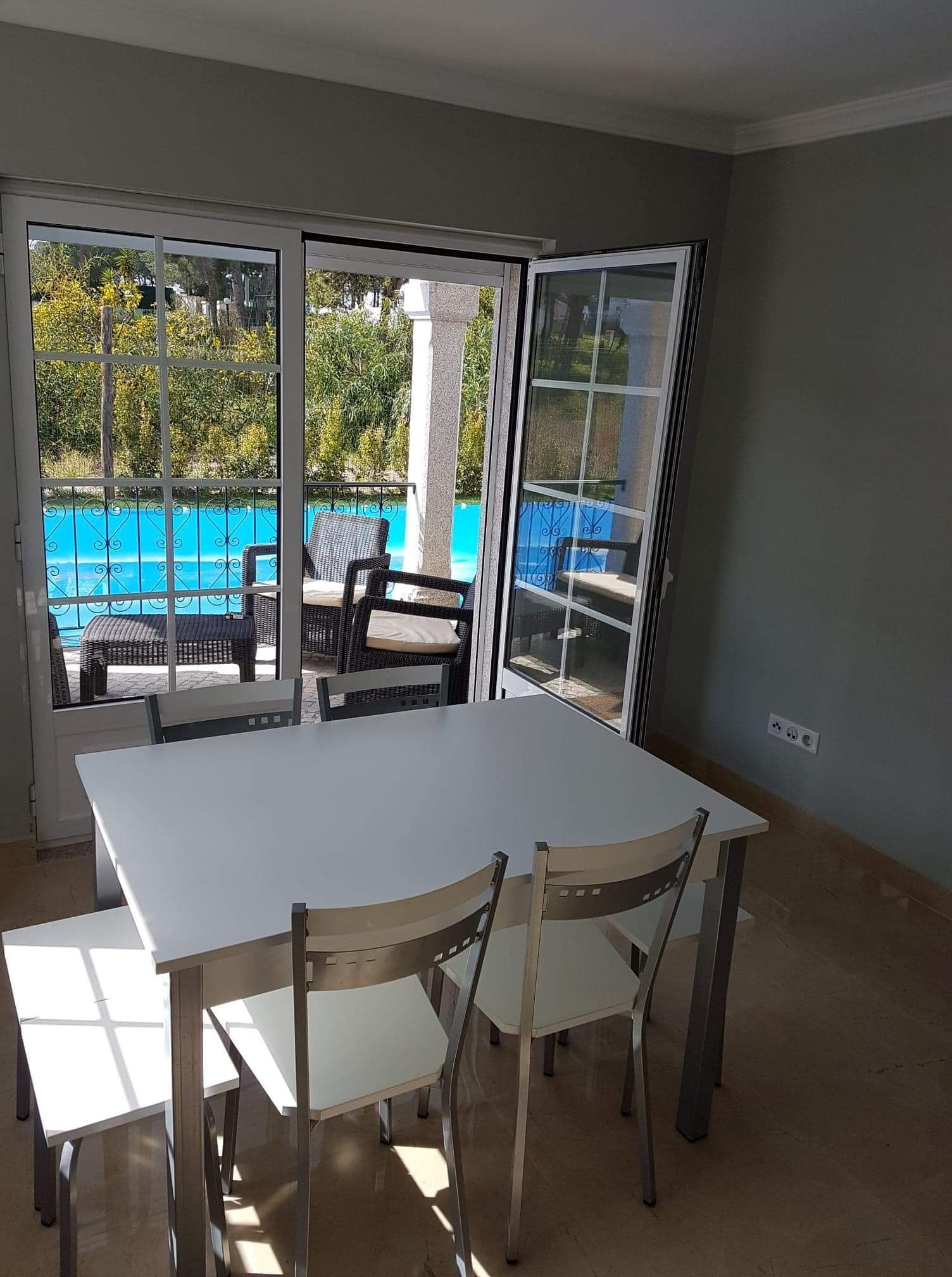 A room with a large table and chairs, a sliding glass door leading to a pool area.