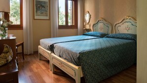 Un letto matrimoniale con testiera floreale, un comodino con una lampada e una finestra con tende.