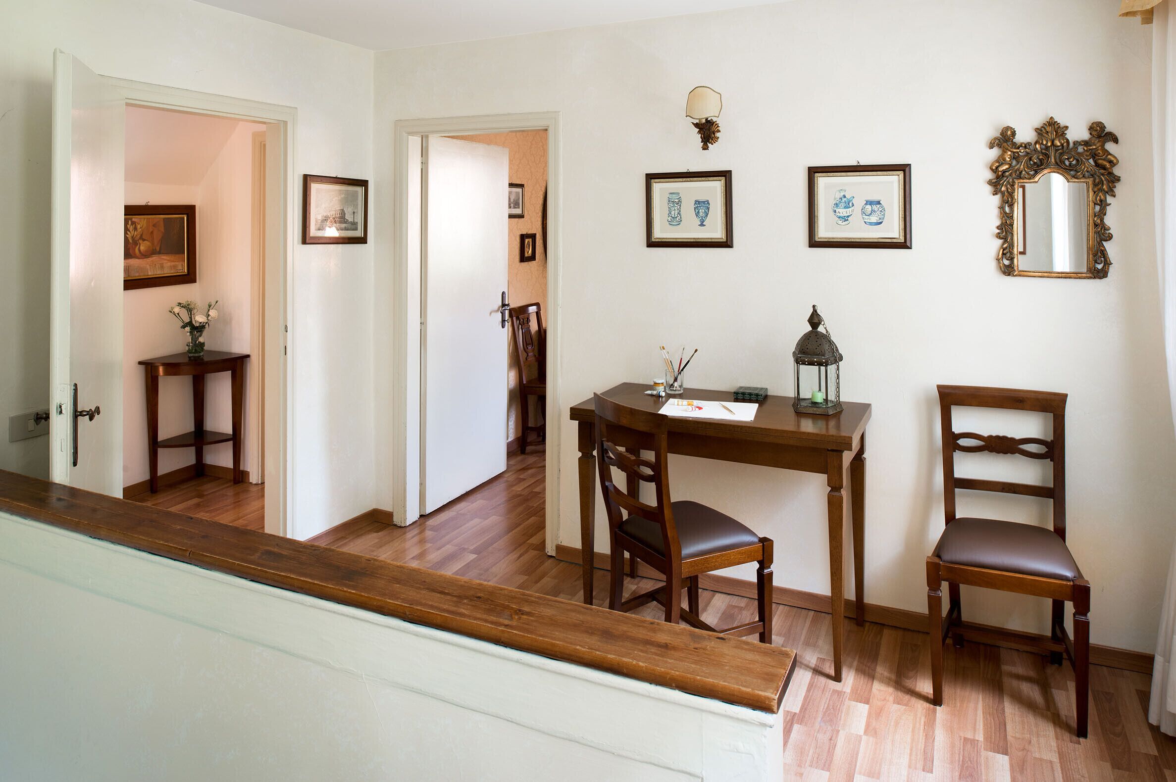Un coin repas avec une table et des chaises en bois, une petite table d’appoint avec un vase, et des tableaux encadrés au mur.