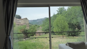 A room with a large window offering a view of a rural landscape, including trees and a stone building.