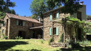 A stone house with a tiled roof, a covered porch, and a garden area.