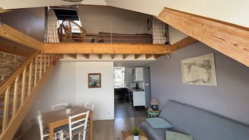 A loft-style living space with a dining area, a kitchen in the background, and a staircase leading to an upper level.
