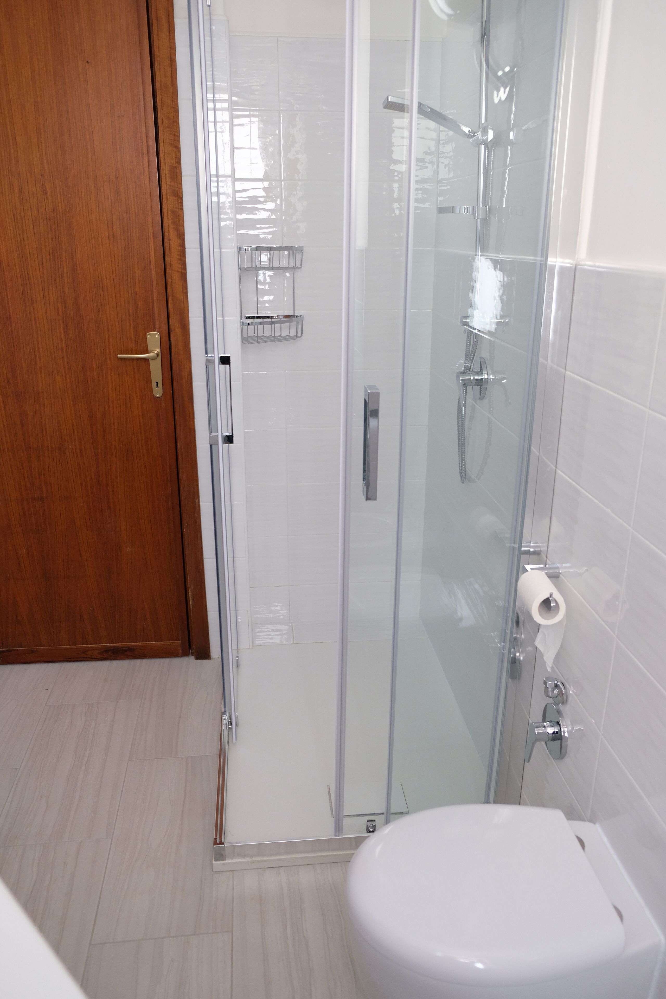 Un bagno moderno con cabina doccia in vetro, un water e una porta in legno.