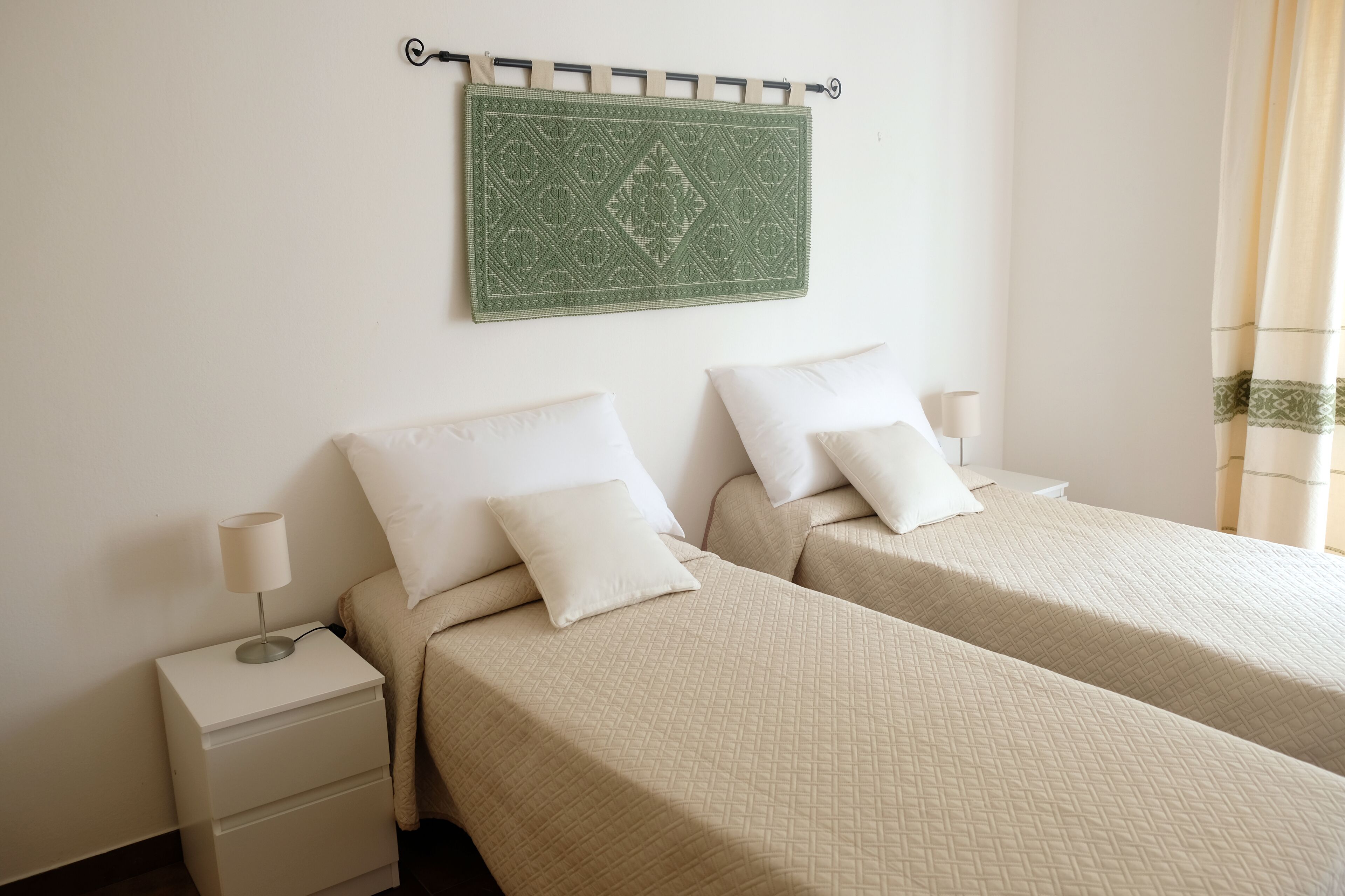 A hotel room with two beds, a nightstand with a lamp, and a decorative wall hanging.