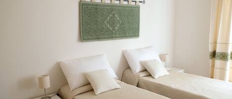 A hotel room with two beds, a nightstand with a lamp, and a decorative wall hanging.