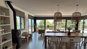 Un comedor moderno con una mesa grande y sillas, una estufa integrada y ventanas amplias que ofrecen vistas al exterior.