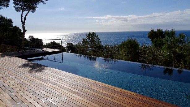 Una piscina infinita con terraza de madera, con vistas a un paisaje marino.