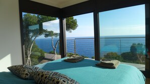 Un dormitorio con una cama grande, vista al mar y un balcón con barandilla.