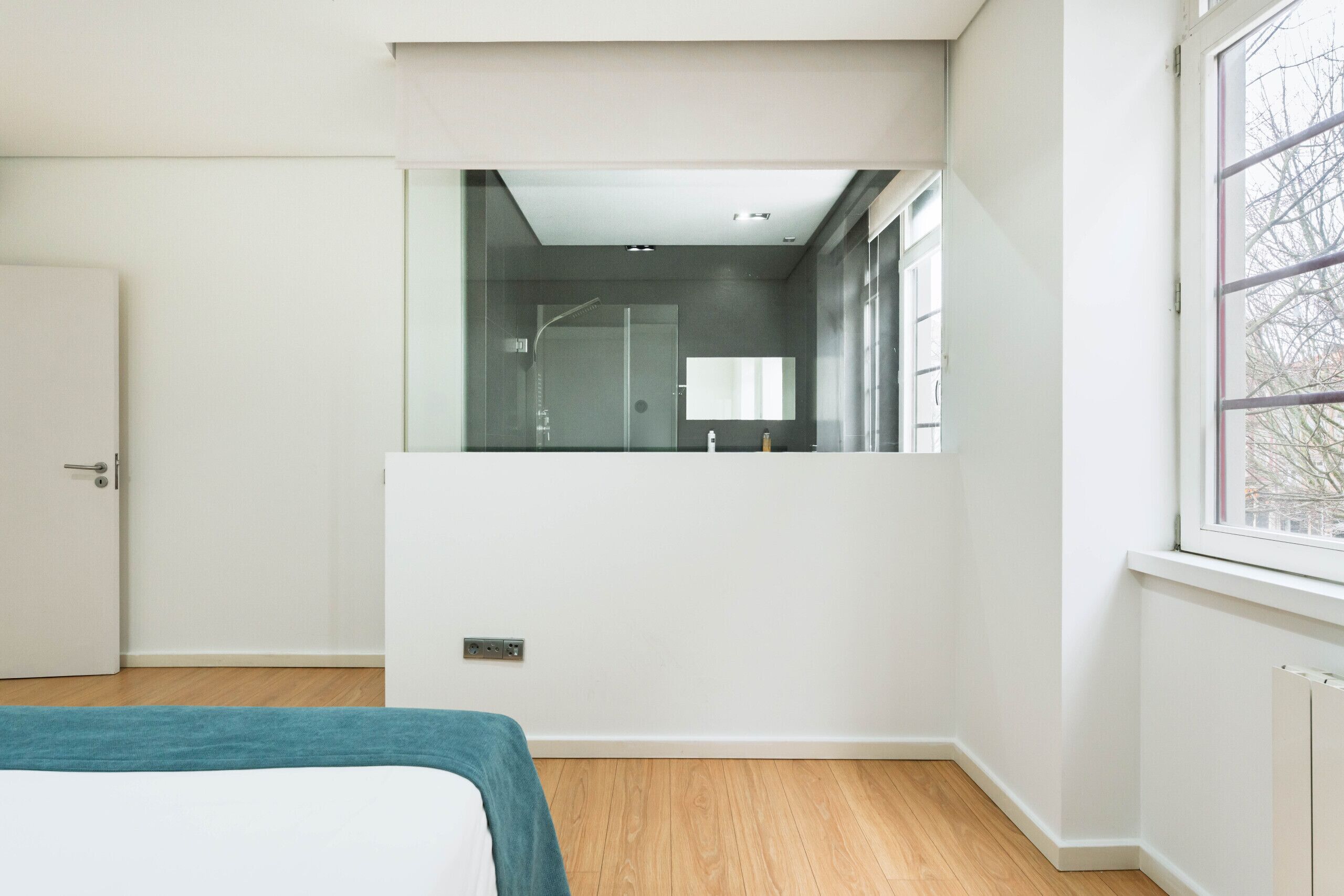 A modern bedroom with a large bed, a mirror, a shower, and a window.
