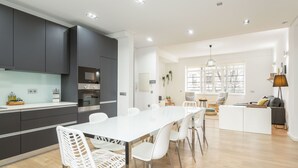 A modern kitchen with dark cabinets, a white dining table, and a seating area with a sofa and chairs. - Feel Porto Downtown Heaven (Oporto)