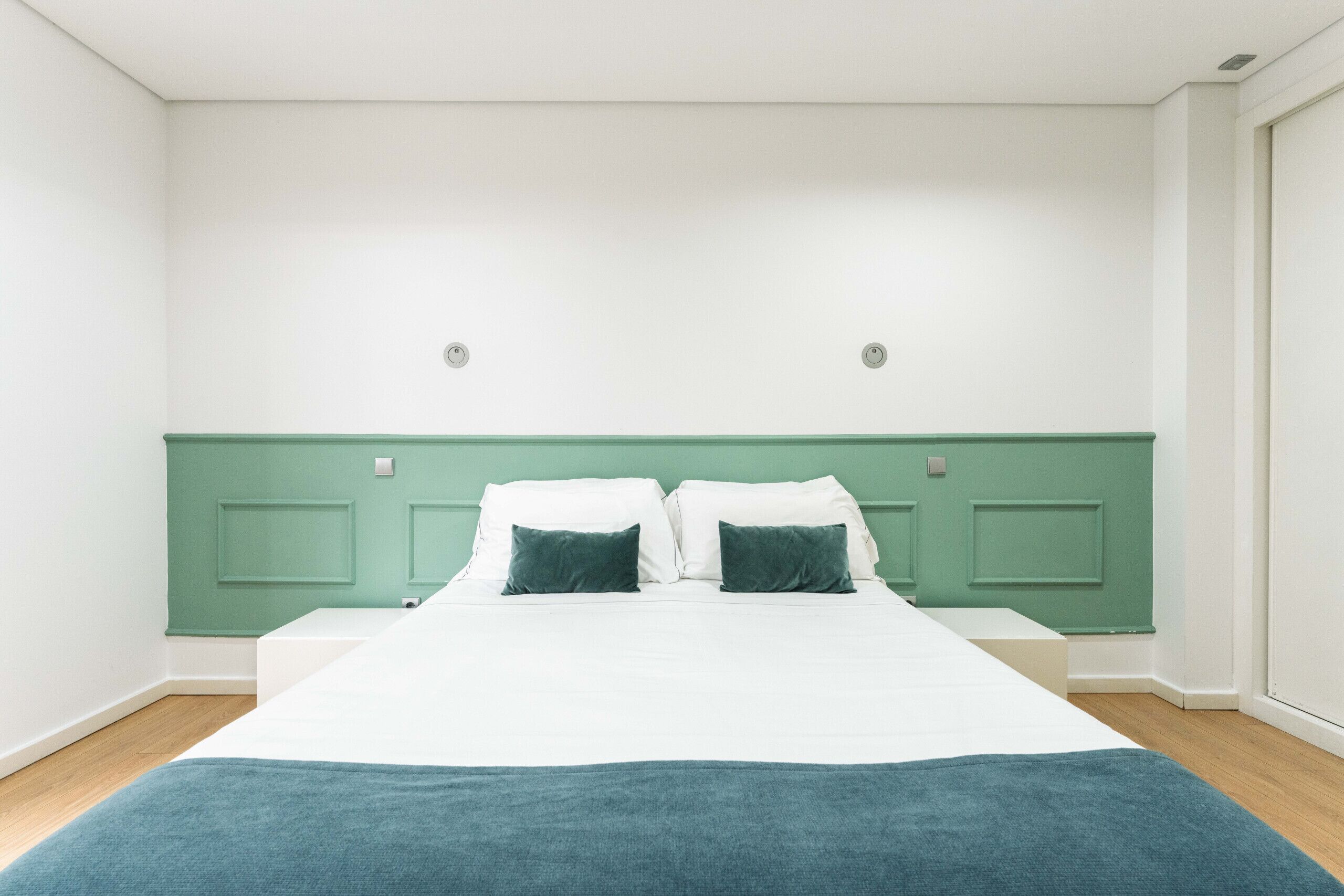 Un dormitorio con cama, cabecera verde, paredes blancas y suelo de madera.