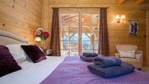 Ein gemütliches Holzblockhaus-Zimmer mit einem Bett, einem Sessel und Blick ins Freie.