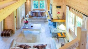 Eine geräumige Holz-Blockhütte mit einer zentralen Sitzecke, einem Esstisch und einer Treppe.