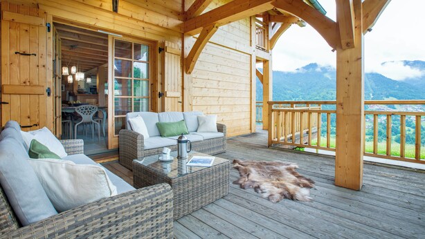 Eine Holzterrasse mit Korbmöbeln, einem Couchtisch und einem Fellteppich.