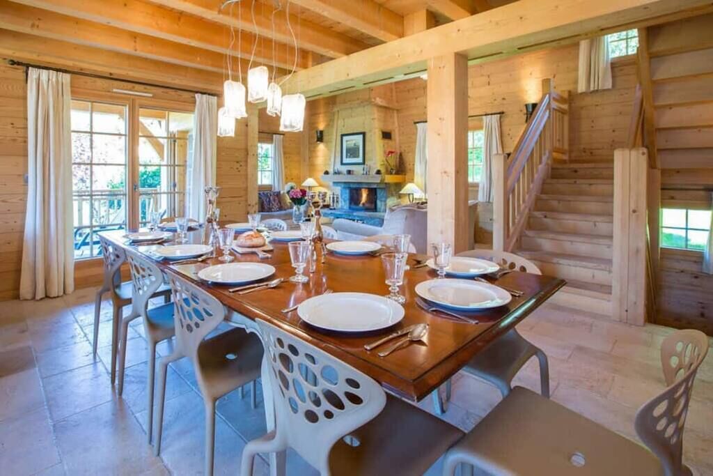 Una cabaña de madera con comedor dispuesto para cuatro, chimenea y escalera.