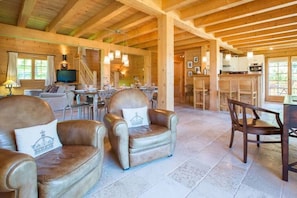A wooden interior with leather armchairs, a dining area, and a kitchen.