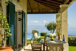 Une terrasse extérieure avec une table dressée pour le repas, offrant une vue panoramique sur la mer et les montagnes.