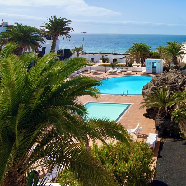 A pool area with a view of the sea, surrounded by palm trees and lounge chairs.