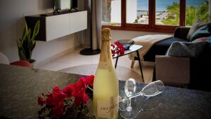 A bottle of Freixenet wine, a glass, and red flowers on a table in a room with a view of the sea.