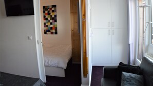 A bedroom with a bed, a TV mounted on the wall, a colorful artwork, a wardrobe, and a window with curtains. - VERY NICE 2-ROOM APARTMENT FOR 4/5 PEOPLE, RECENTLY REFURBISHED (Morzine)