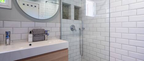 A modern bathroom with white subway tiles, a round mirror, a glass-enclosed shower, and a wooden vanity.
