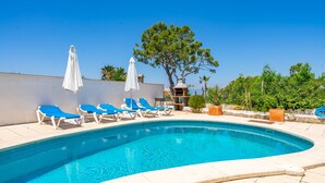 A swimming pool with blue lounge chairs and white umbrellas, surrounded by a stone wall and trees. - Villa Bahías - with private swimming pool (Bahía Grande)