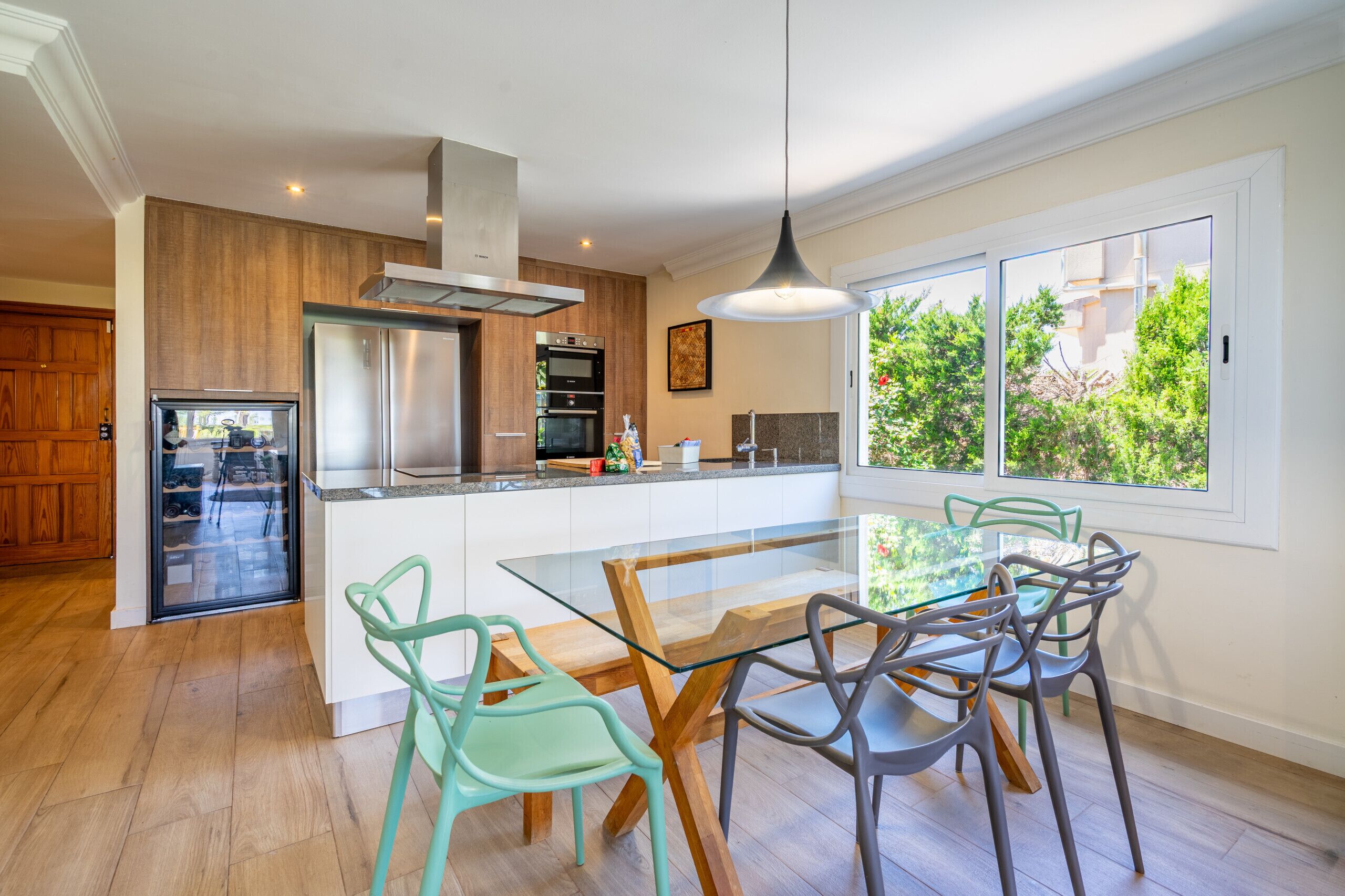 A modern kitchen with a central island, wooden cabinets, and a glass dining table with chairs.