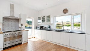 A modern kitchen with a stainless steel stove, white cabinets, and a large window offering a view of the countryside. - Large Luxury House with Heated Pool, Hot Tub, Cinema close to coast near Shaldon (Stokeinteignhead)