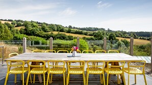 A wooden table with yellow chairs set outdoors, overlooking a hilly landscape with vineyards. - Large Luxury House with Heated Pool, Hot Tub, Cinema close to coast near Shaldon (Stokeinteignhead)