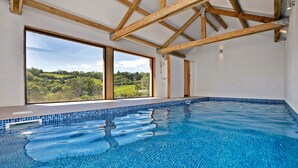 A swimming pool with a view of a green landscape through large windows. - Large Luxury House with Heated Pool, Hot Tub, Cinema close to coast near Shaldon (Stokeinteignhead)