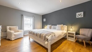 Ett sovrum med en stor säng, två sängbord, en stol och en byrå.