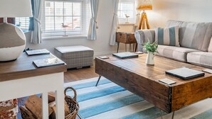 Ett vardagsrum med ett soffbord i trä, en soffa, en lampa och utsikt över omgivningen genom stora fönster.