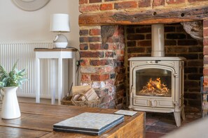 A rustic room with a brick fireplace, a white table with a vase, and a lamp.