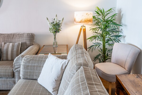 A living room with a sofa, armchair, side table, lamp, vase with flowers, and a large plant.