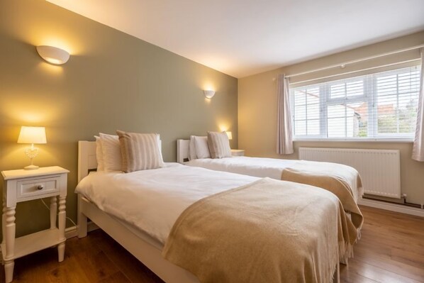 Una habitación con dos camas, una mesita de noche con lámpara y una ventana con persianas.