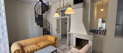A modern living room with a sofa, armchairs, a coffee table, a fireplace, and a spiral staircase.