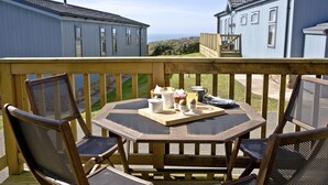 A wooden deck with a table and chairs, overlooking a scenic view of two blue houses. - Luxury 3 bed Lodge In Soar, Salcombe, Devon, Sea & Country views (Salcombe)