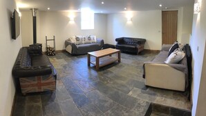 A cozy living room with a fireplace, two sofas, a coffee table, and a stone-tiled floor. - HartHill Grange Bunkhouse - Unique 1850's Rural Country Accommodation (Lydney)